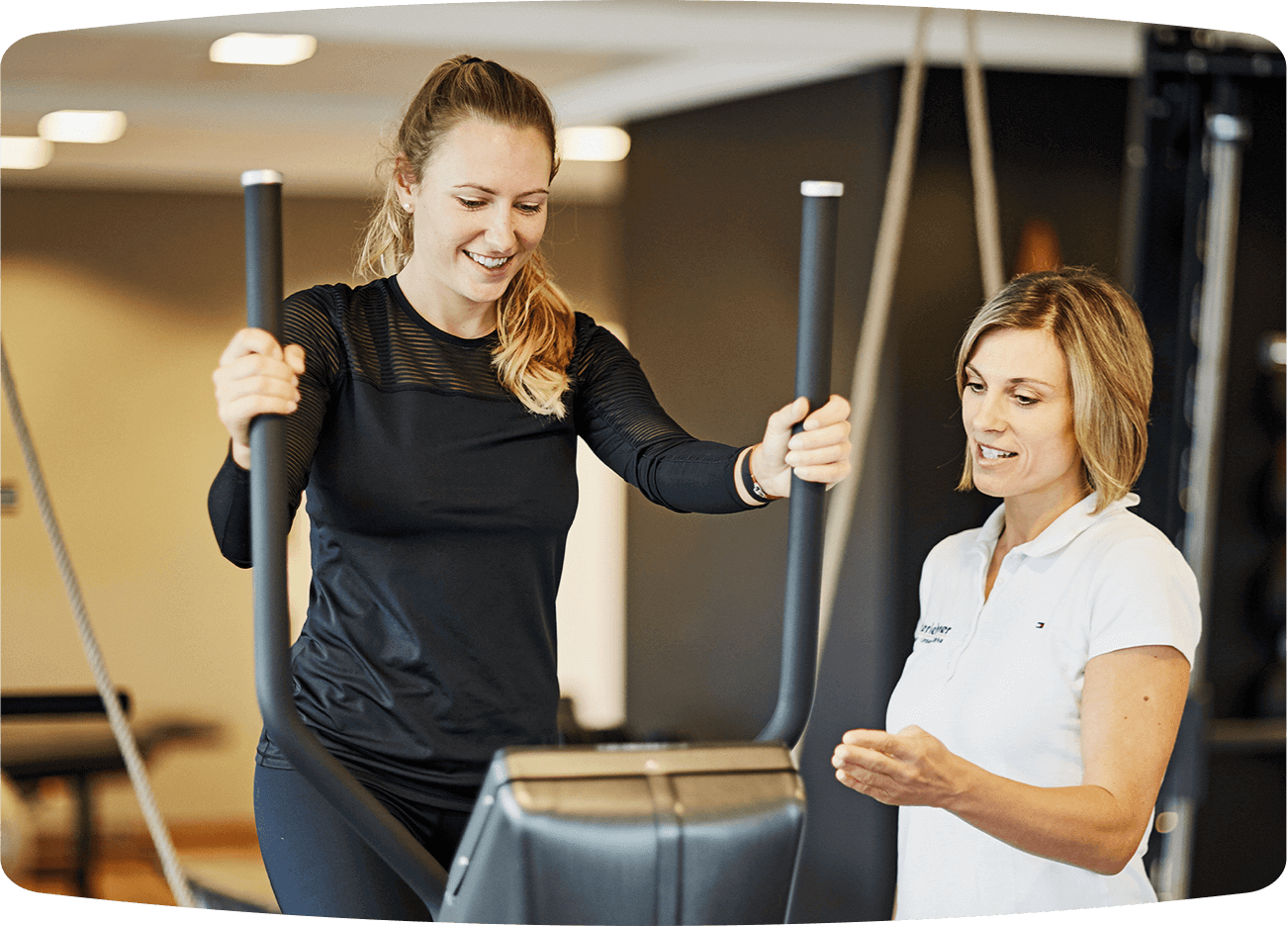 Junge Frau mit Fitnesstrainerin an Fitnessgerät